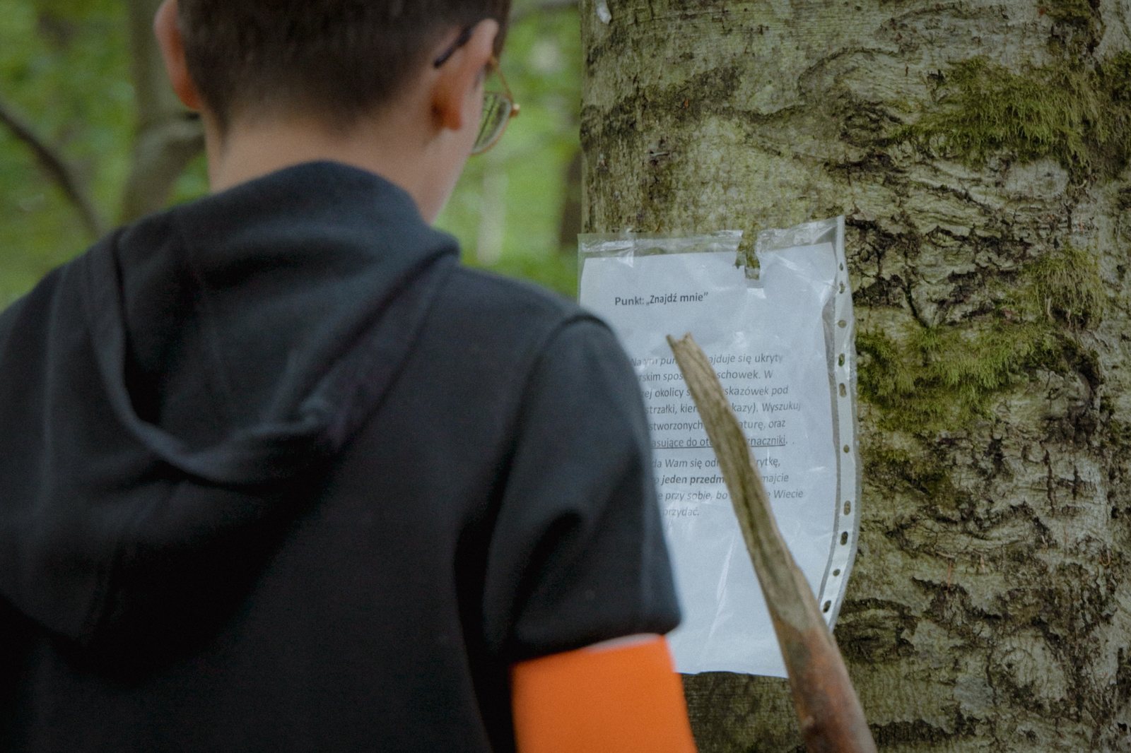 Uczestnik czyta wskazówkę przypiętą do drzewa na trasie