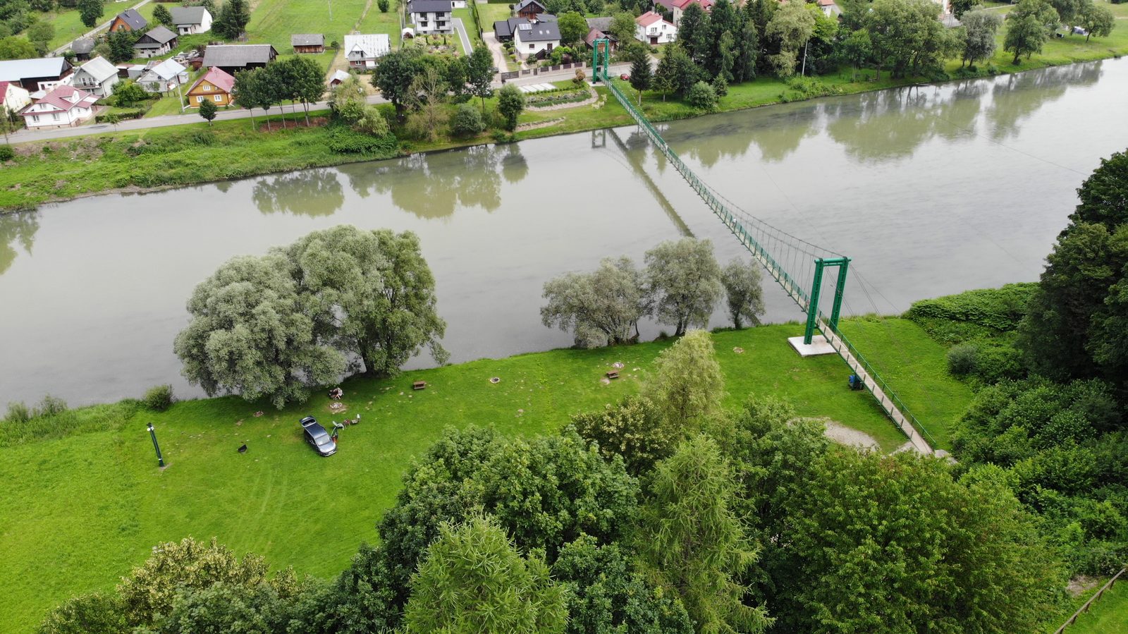 Polana nad rzeką i wisząca kładka - widok z drona