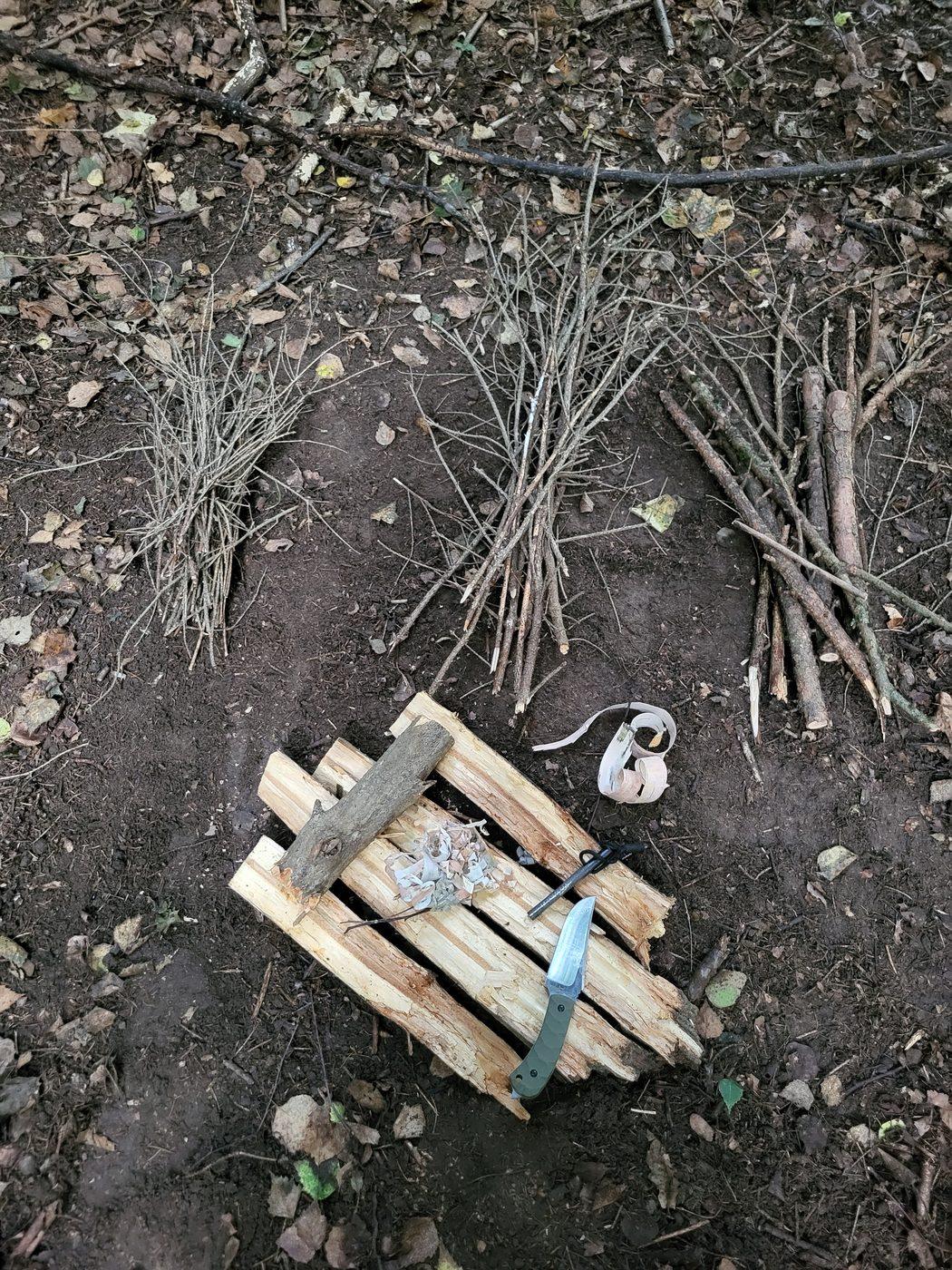 Przygotowane miejsce na ognisko - podkład z drewna, rozpałka, wiórki, krzesiwo i nóż, obok drewno ułożone od najcieńszego